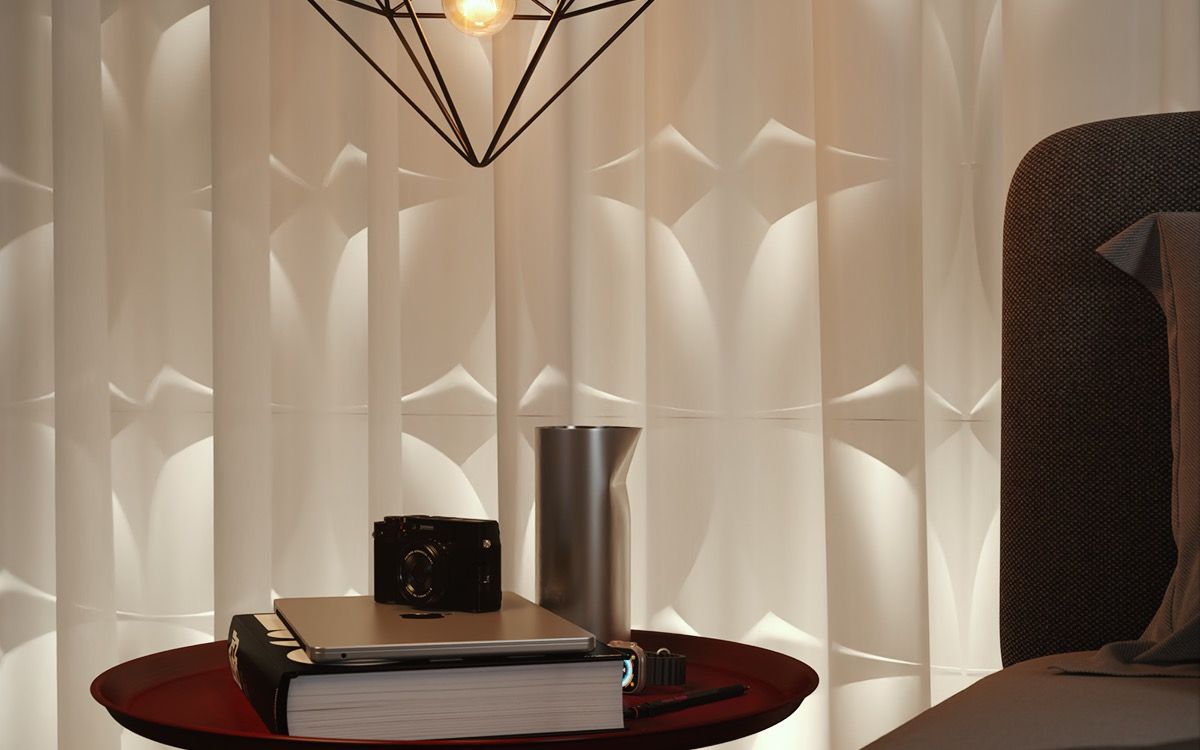 A red topped side table under a faceted black wire pendant, holding a camera, a laptop and a thick book, with a sheer curtain and a sculpted white wall panel behind.